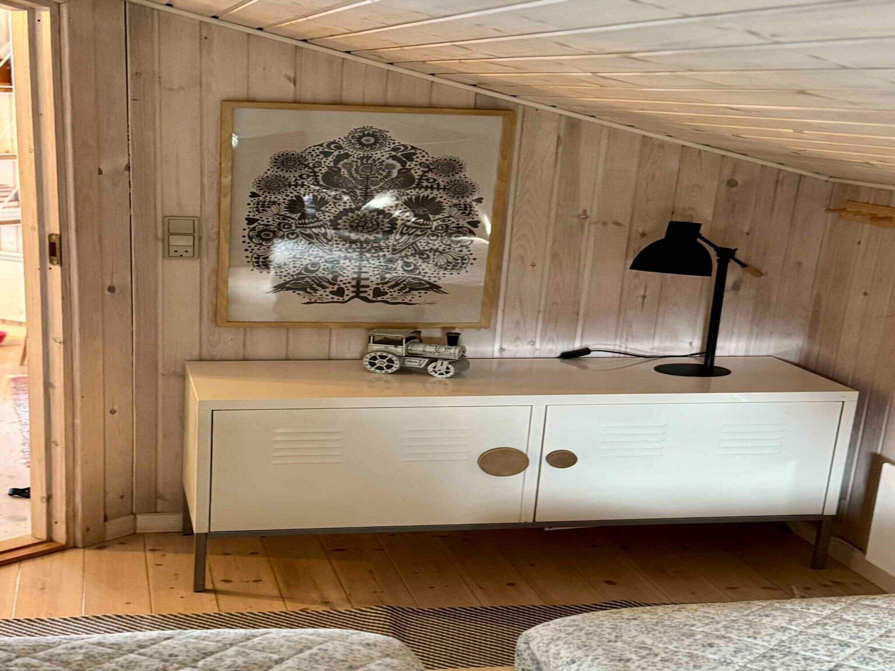 A room with a white cabinet, a framed black and white floral artwork, a toy train, and a desk lamp.