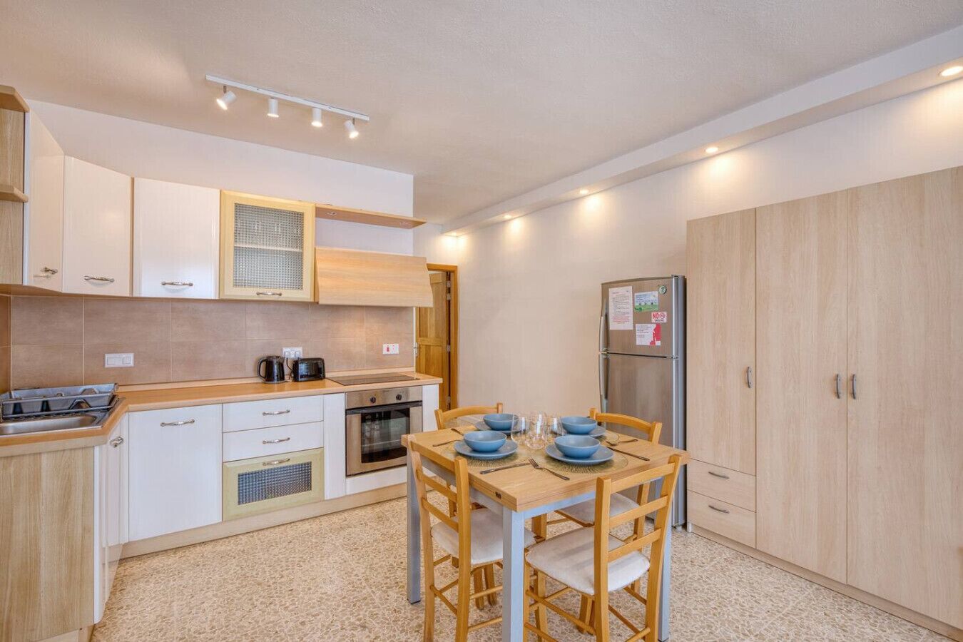 A compact kitchen with white cabinets, a wooden countertop, a dining table with blue bowls, and a refrigerator.