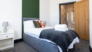 A neatly made bed with a grey headboard, white bedding, and a black throw blanket. There is a wooden door to the right and a white nightstand with a lamp to the left. - Luxury 2 Bedroom & 2 Bathroom Central Flat (Swansea)