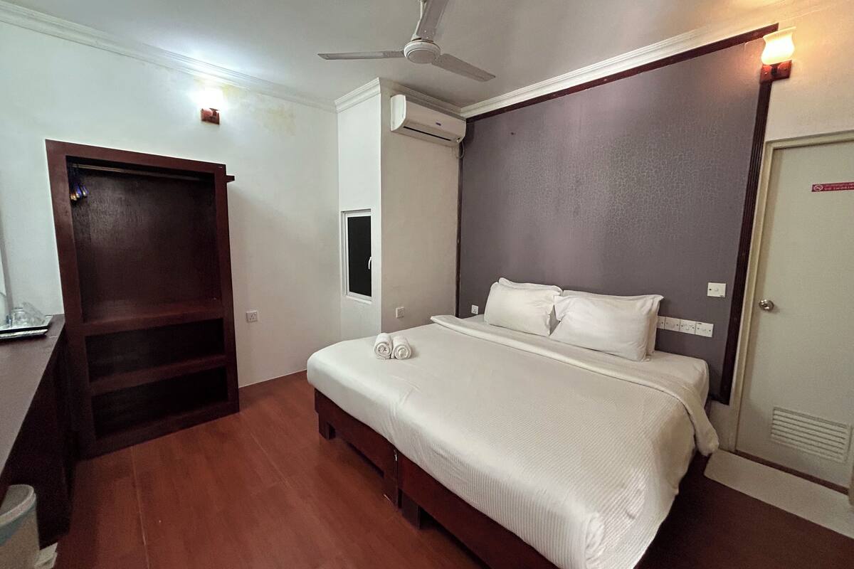 Een slaapkamer met een bed, een plafondventilator, een airconditioning en een houten kledingkast.