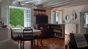 Un comedor acogedor con una mesa redonda y sillas, un televisor y una zona de cocina con un armario y estanterías.