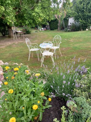 A garden with a white metal table and chairs, surrounded by various plants and flowers. - Wellness Cottage. Massage therapist on site for a true resource. (Forges de Lanouée)