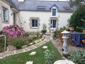 A garden with a stone pathway leading to a white door, surrounded by various plants and flowers. - Wellness Cottage. Massage therapist on site for a true resource. (Forges de Lanouée)
