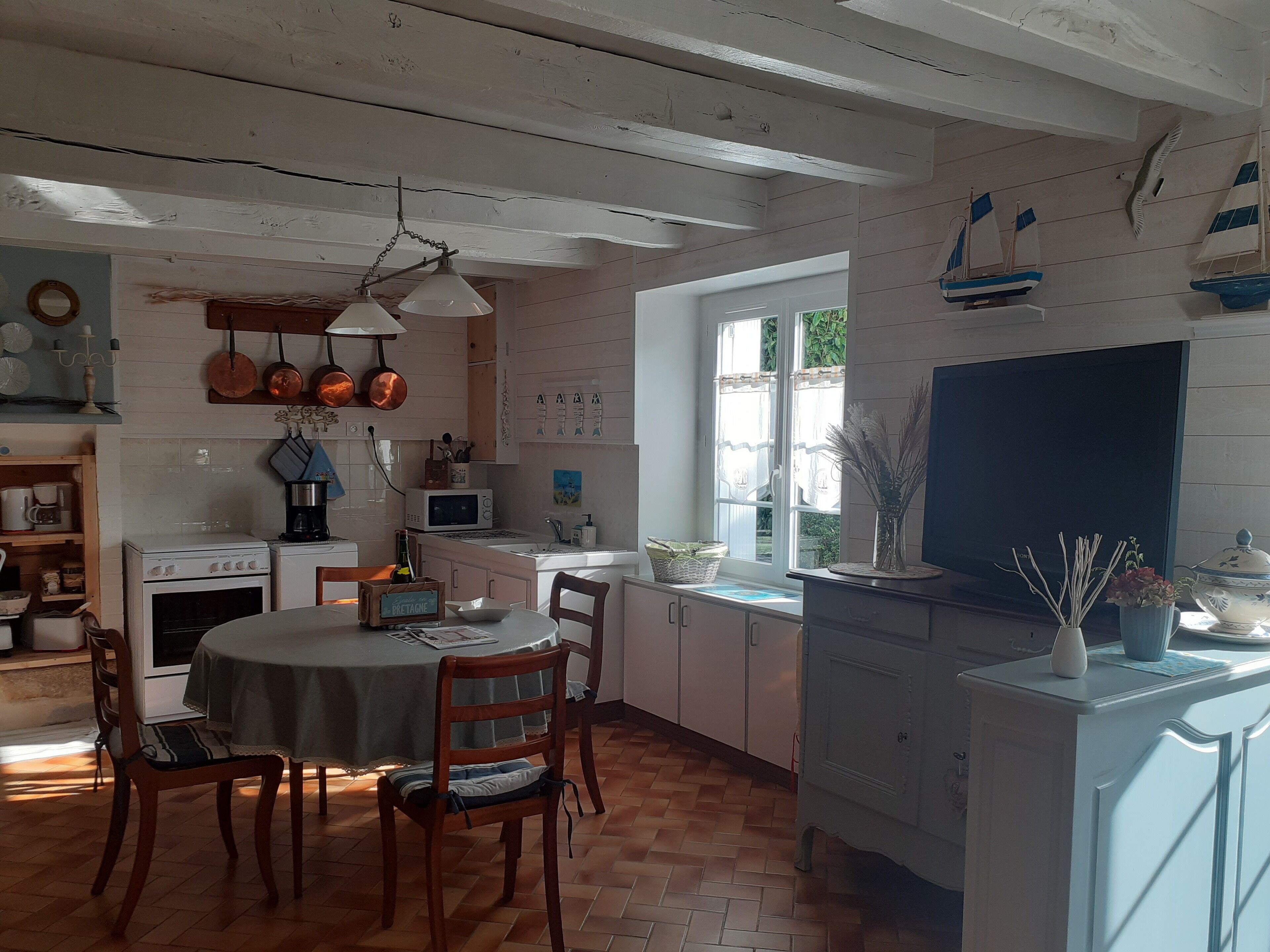 Une cuisine avec des meubles en bois, une table à manger et des chaises. Une fenêtre offre une vue sur la verdure à l’extérieur.
