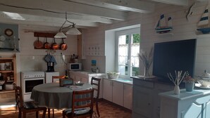 Cocina con armarios de madera, una mesa de comedor y sillas. Se ve un ventanal con vistas a la vegetación.