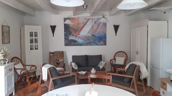 A cozy living room with a large painting of sailboats, a sofa, and two wooden chairs. - Wellness Cottage. Massage therapist on site for a true resource. (Forges de Lanouée)