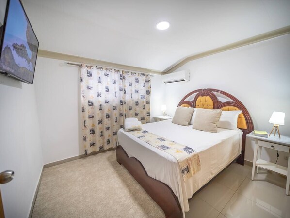 A hotel room with a bed, a nightstand, a lamp, a TV, and a curtain with a nautical theme.