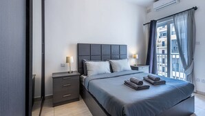 A modern bedroom with a large bed, bedside tables, and a view of the city through the window. - The Fives Apartment - St Julians (St. Julian`s)