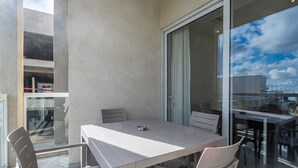A balcony with a white table and chairs, a glass door, and a view of the cityscape. - The Fives Apartment - St Julians (St. Julian`s)