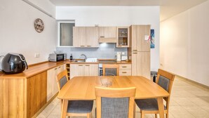 A modern kitchen with wooden cabinets, a dining table with chairs, a kettle, a microwave, and a sink. - The Beach Apartment - Sliema (Sliema)