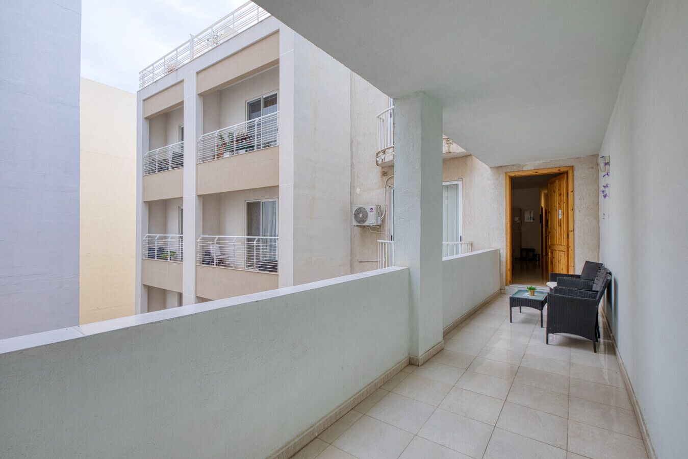 A corridor with a balcony, a small seating area, and a door leading to another room.