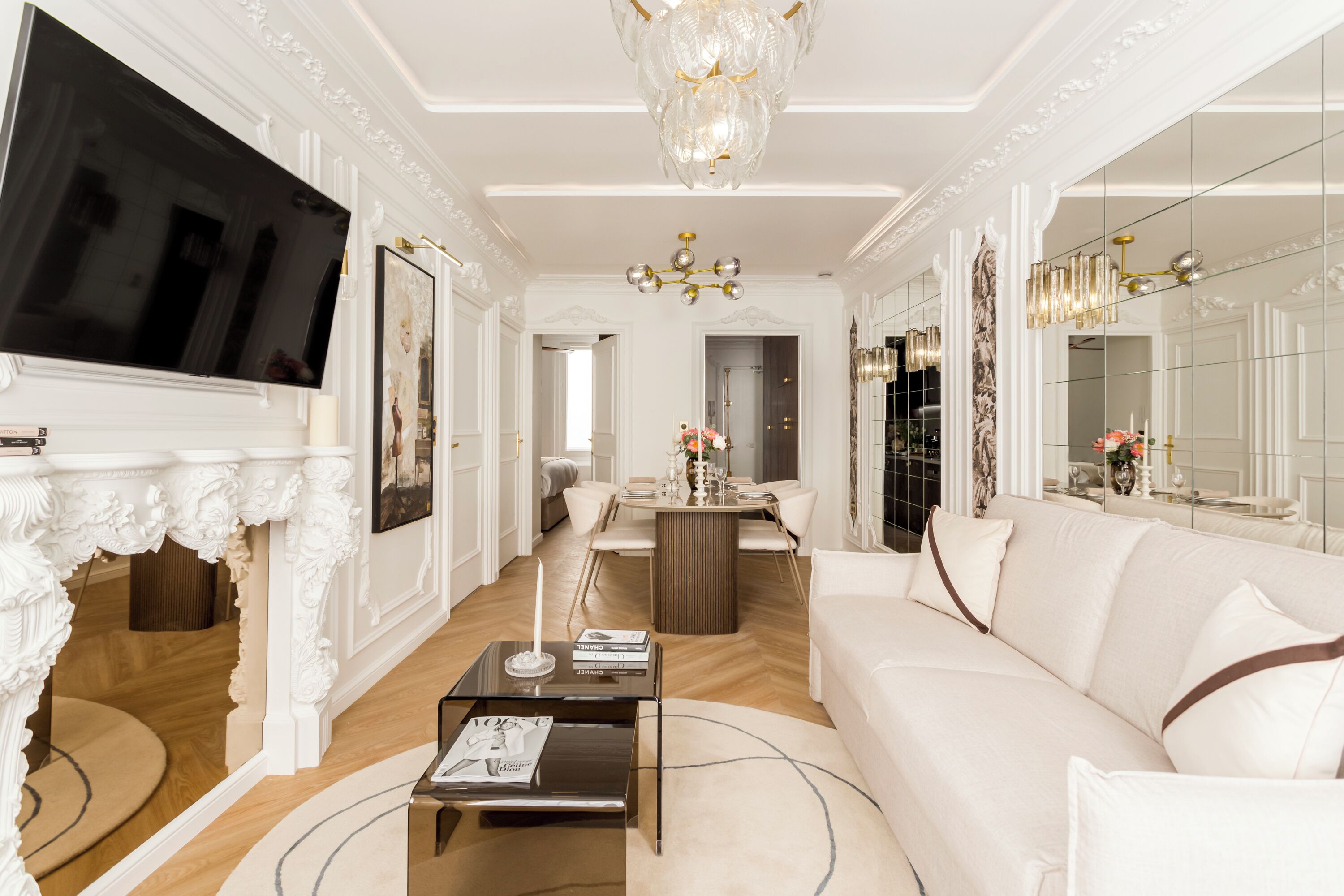 A spacious living room with a large flat-screen TV, a fireplace, a chandelier, and a dining area.
