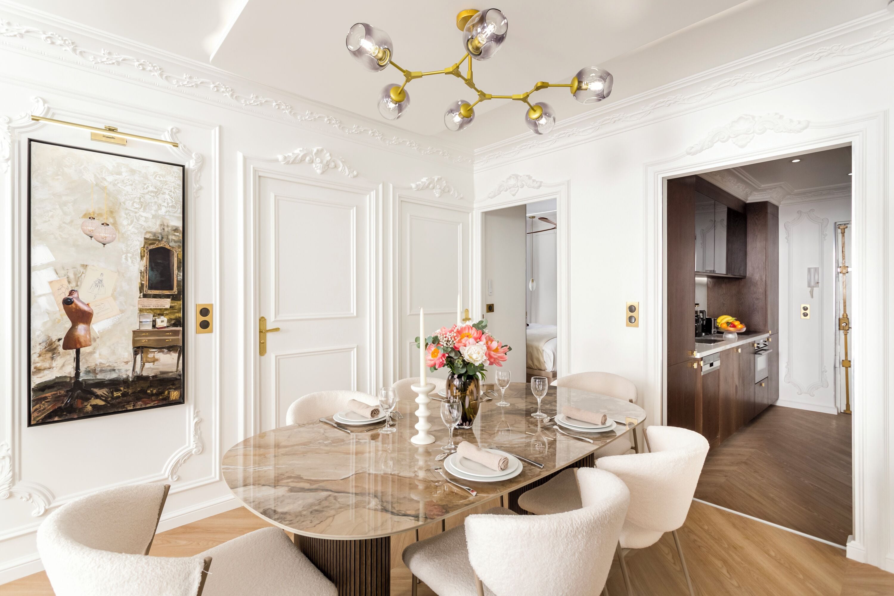 A dining area with a marble table, white chairs, a chandelier, and a framed artwork on the wall.