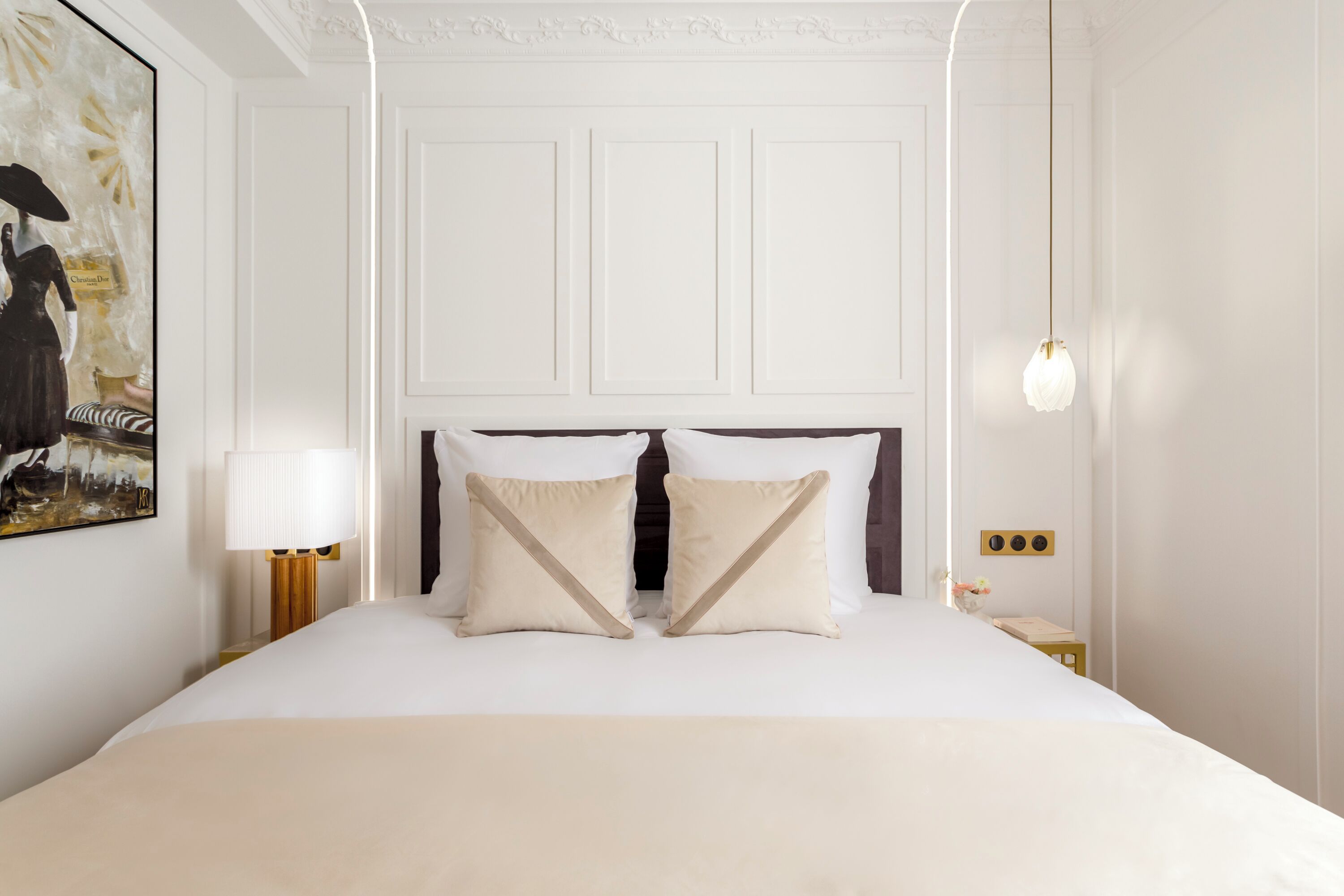 Una habitación de hotel con una cama grande, paredes blancas, un cabecero de madera y una mesita de noche con lámpara.