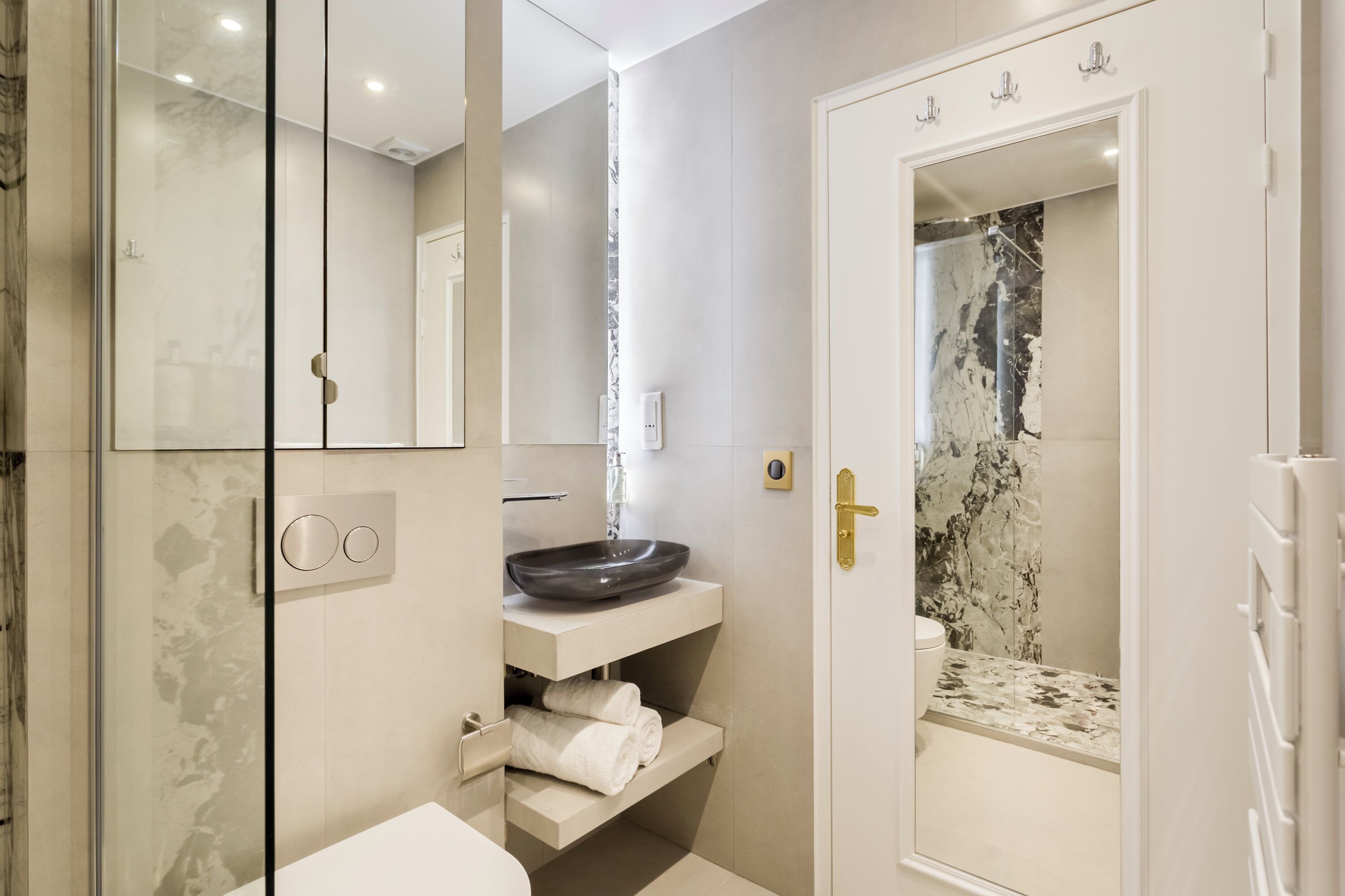 A modern bathroom with a glass shower enclosure, a white sink with a marble countertop, and a white vanity with a towel rack.