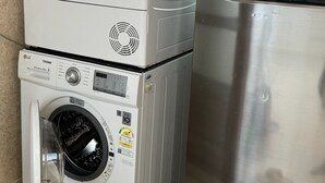 Un angolo lavanderia funzionale con lavatrice a carica frontale, asciugatrice impilata e frigorifero in acciaio inossidabile.