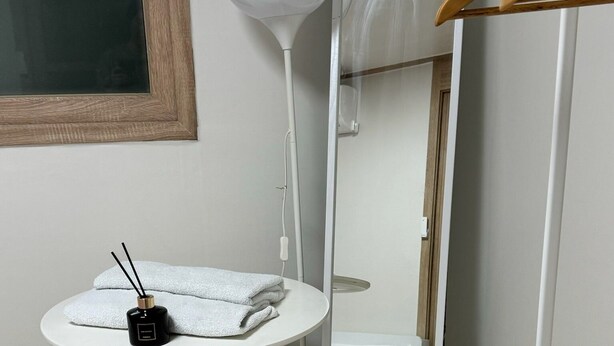 Una stanza piccola con un tavolo bianco rotondo, uno specchio, un appendiabiti e un letto.