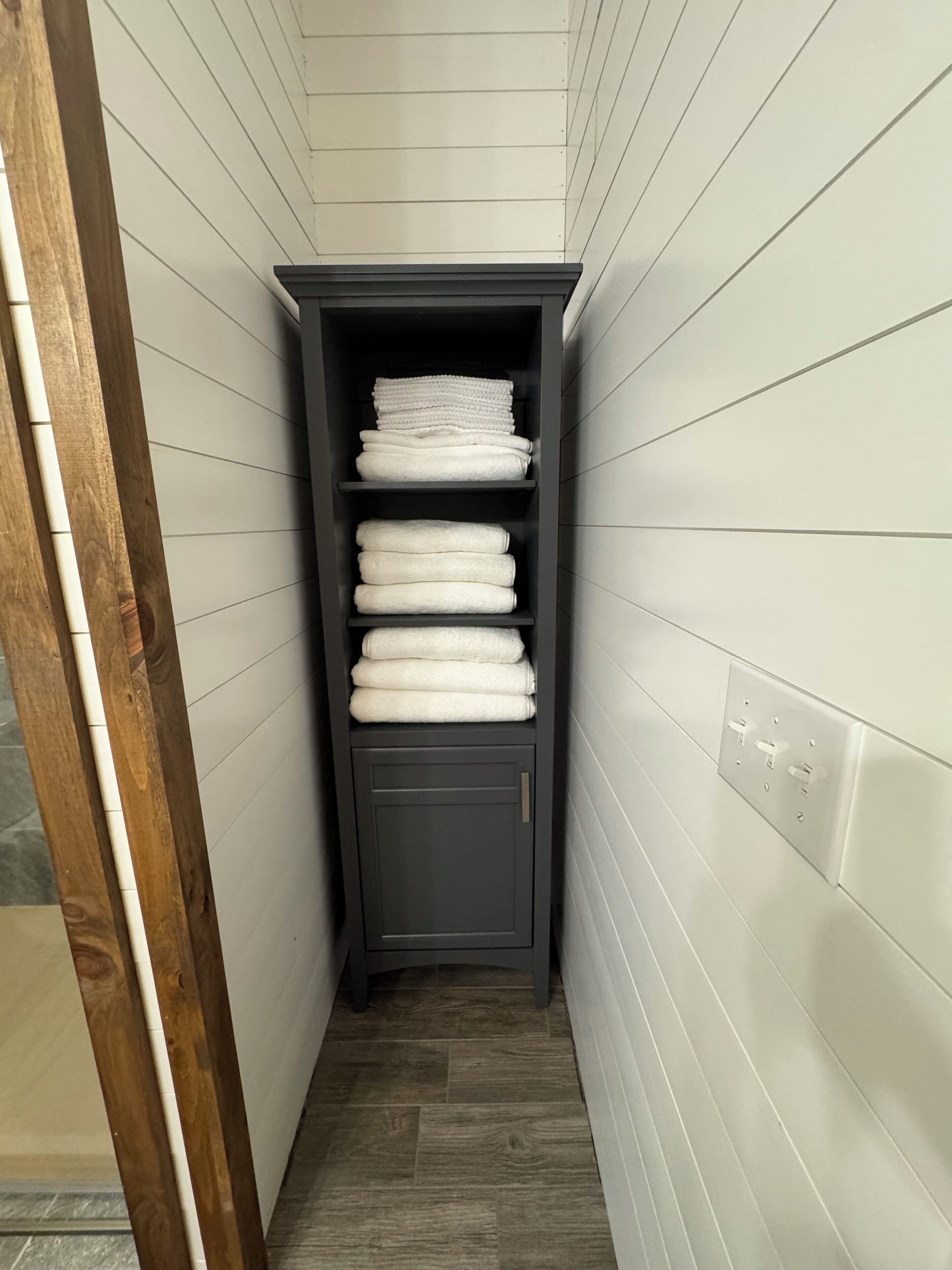 A narrow hallway with a dark wooden cabinet containing neatly folded white towels.