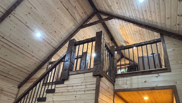 L’intérieur d’une cabane en bois comprend une chambre à coucher située en mezzanine, un escalier et une porte donnant sur une pièce lumineuse.