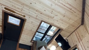 L’intérieur d’une cabane avec un plancher en bois, un canapé marron agrémenté de coussins, une petite table et un escalier.