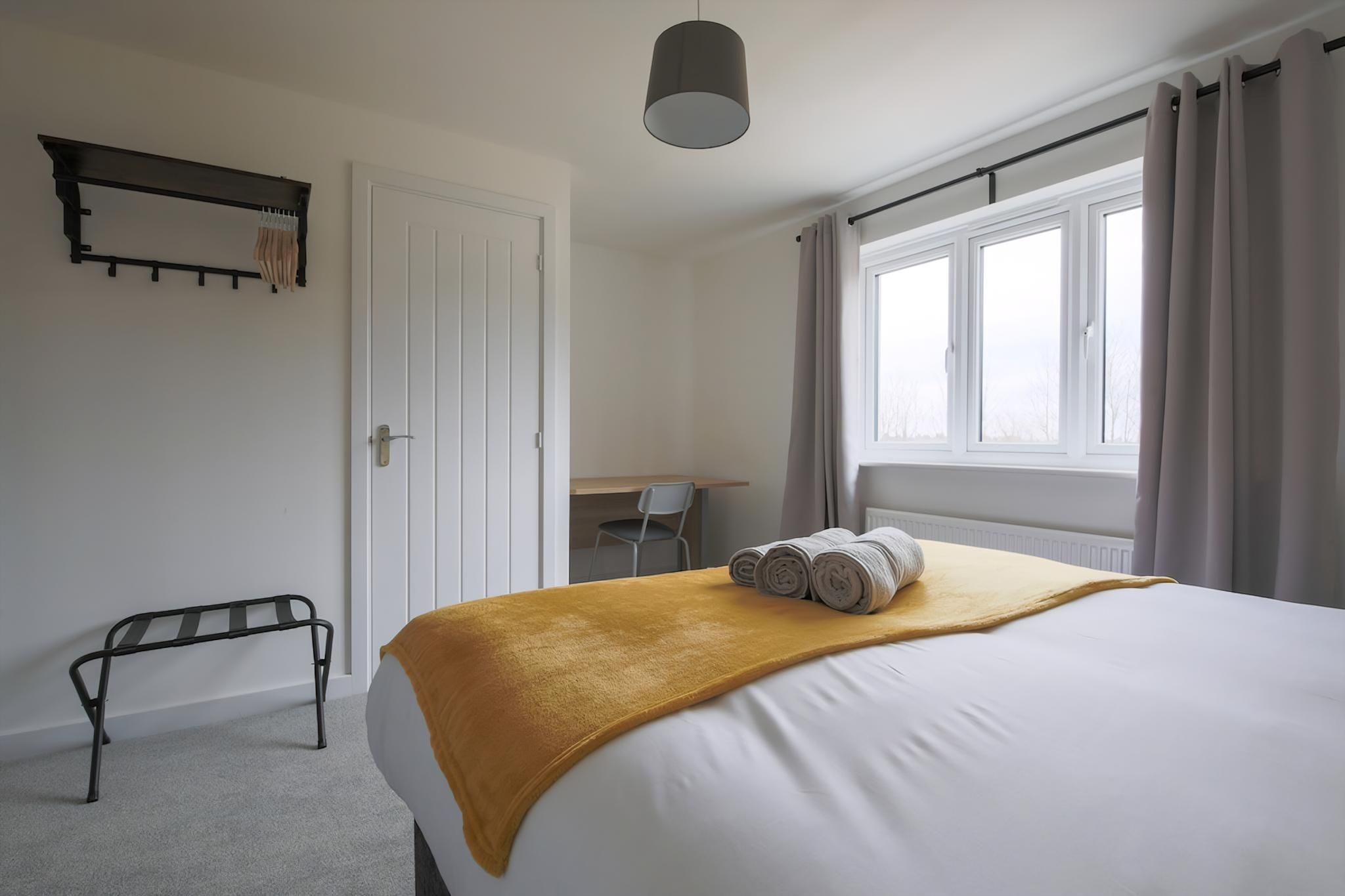 Habitació d'hotel amb llit, escriptori, cadira, banca i finestra amb cortines.