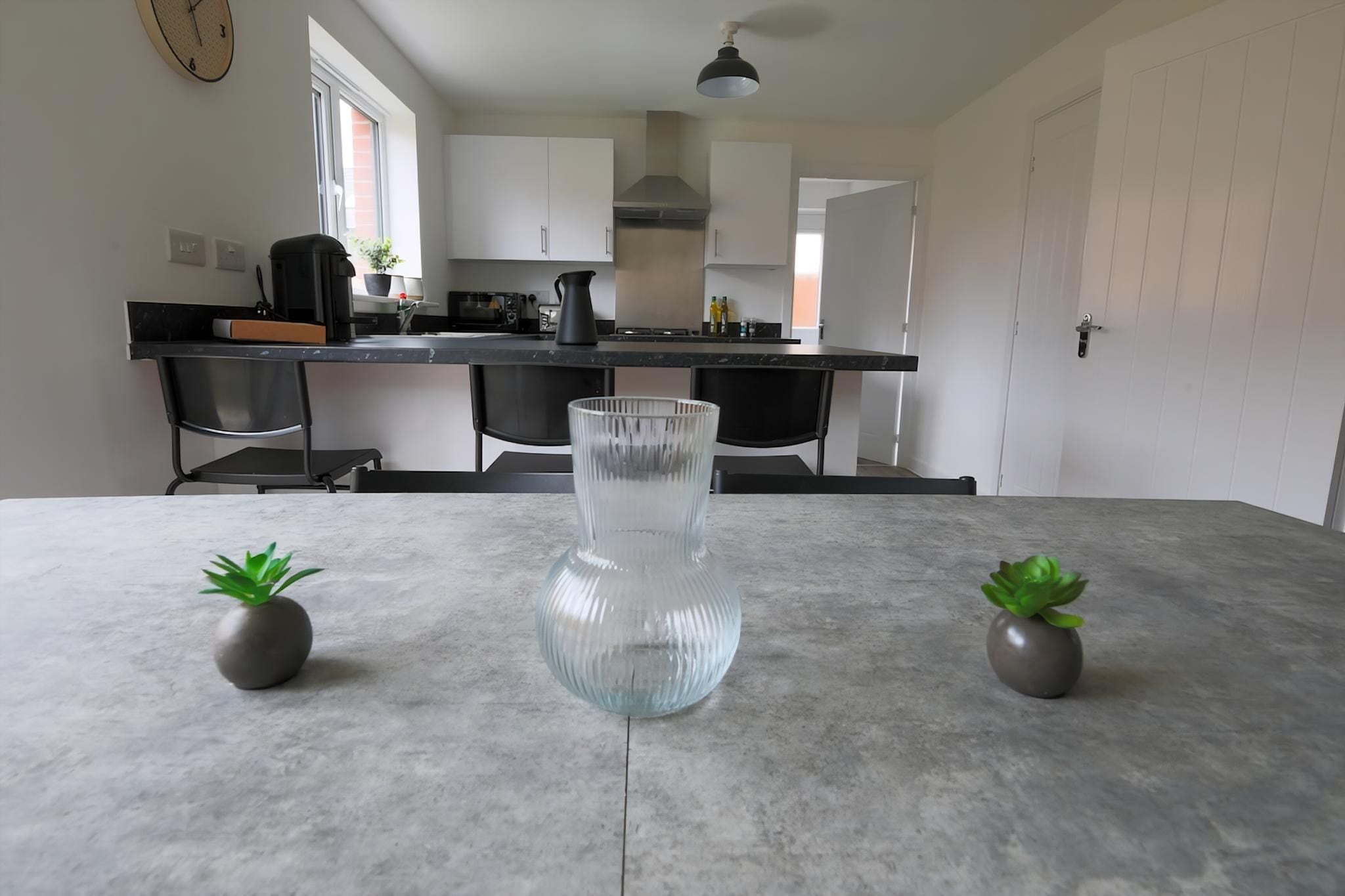 A modern kitchen with white cabinets, a black countertop, and a clear glass vase on the table.