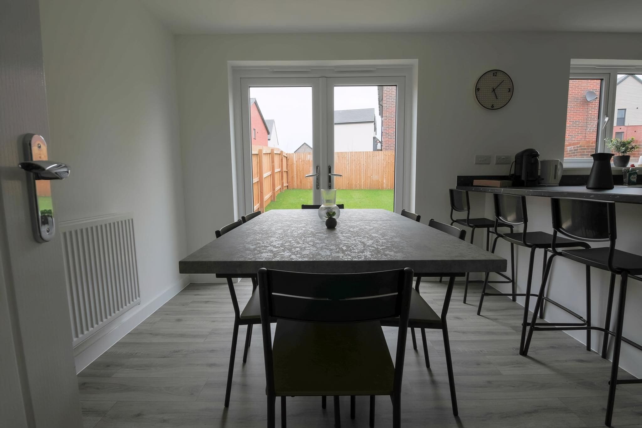 Una cocina moderna con una mesa de comedor, sillas, un reloj y vistas a un patio trasero.