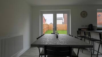 A dining area with a table and chairs, a window with a clock, and a view of a backyard.