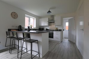 Uma cozinha moderna com ilha central, banquetas, um relógio e uma janela.