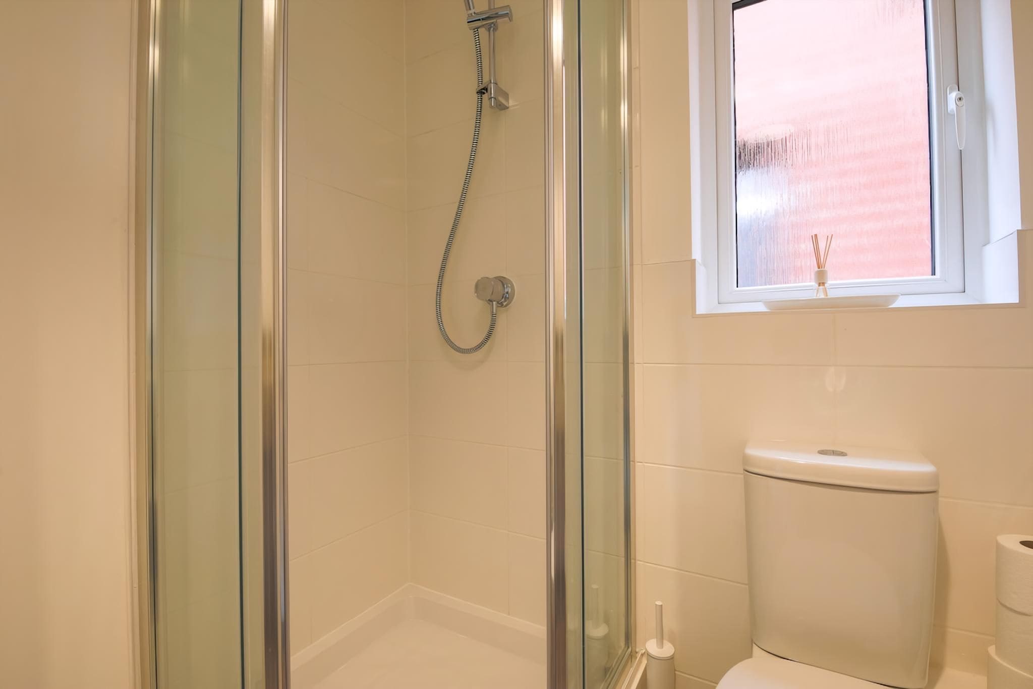 A bathroom with a glass-enclosed shower, a toilet, and a window.