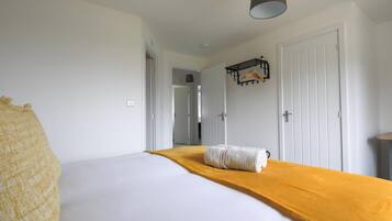A hotel room with a bed, a yellow throw blanket, a hanging light fixture, and a coat rack.
