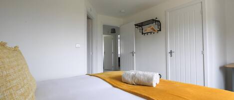 Habitación de hotel con una cama, un plaid amarillo, una lámpara colgante y un perchero.