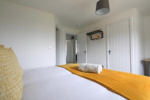 Quarto de hotel com uma cama, um cobertor amarelo, luminária pendente e um porta-roupas.