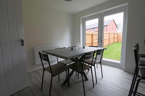A dining area with a table and chairs, a radiator, and a view of a backyard through a large window. - The Haven Modern 4-bed Home With Garden (Cardiff)