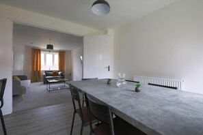 Uma cozinha moderna com bancada de mármore, sala de jantar com mesa e cadeiras, e sala de estar com sofá e janela com cortinas.