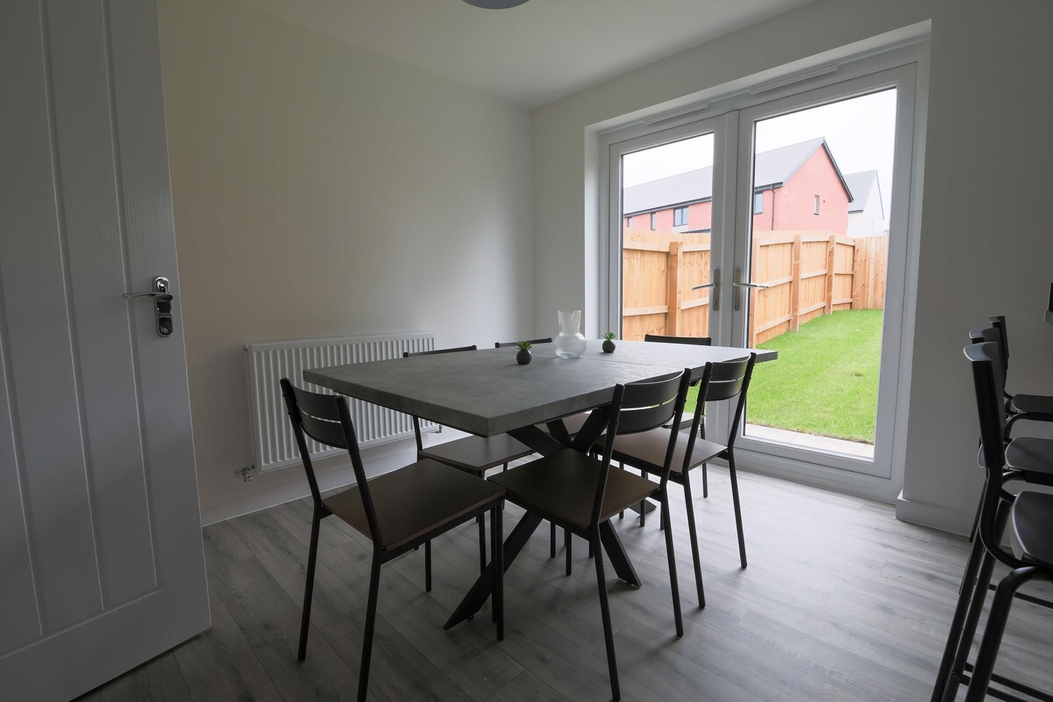 A dining area with a table and chairs, a radiator, and a view of a backyard through a large window.