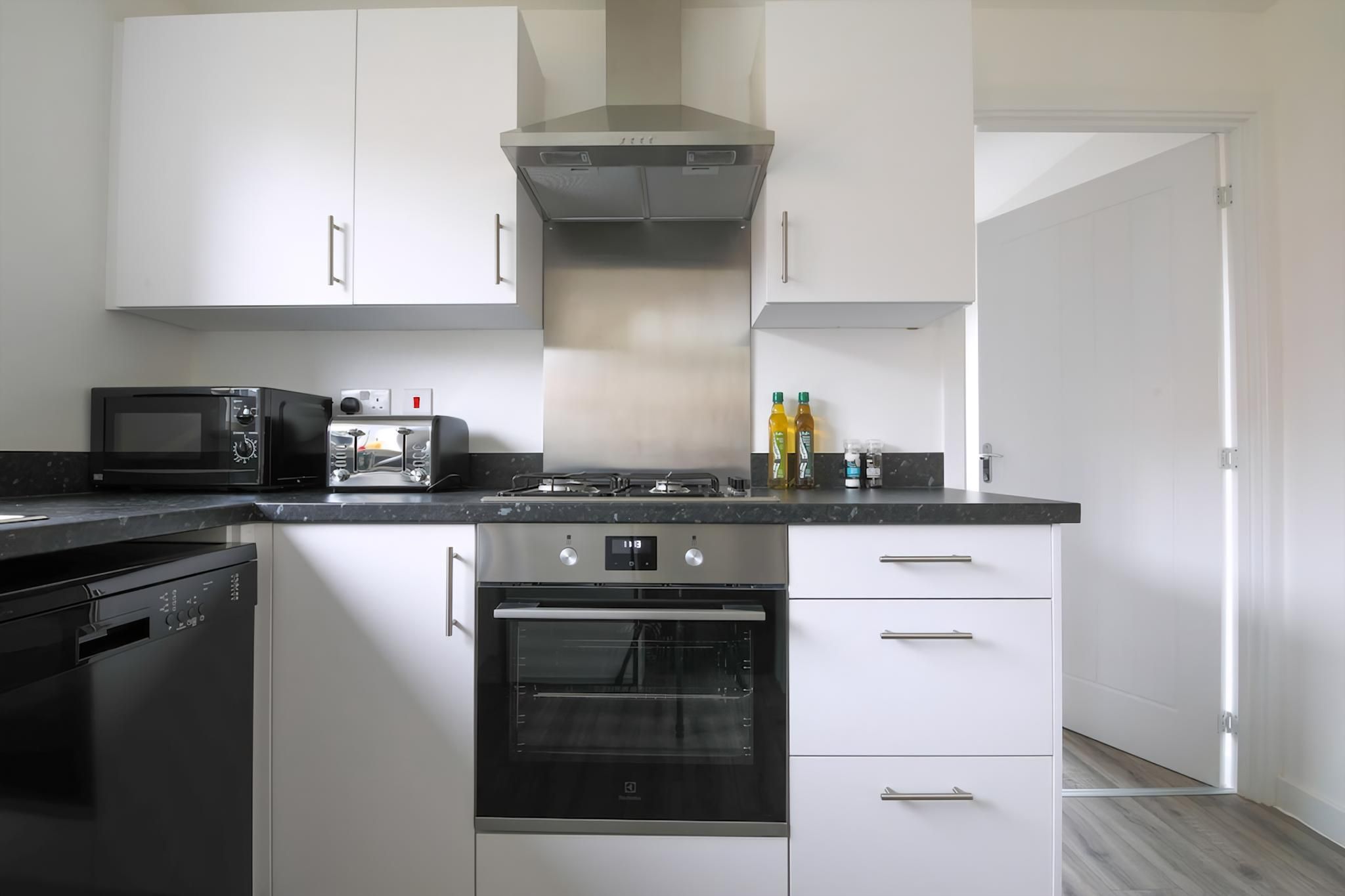A modern kitchen with white cabinets, a black dishwasher, a microwave, an oven, and a gas stove.