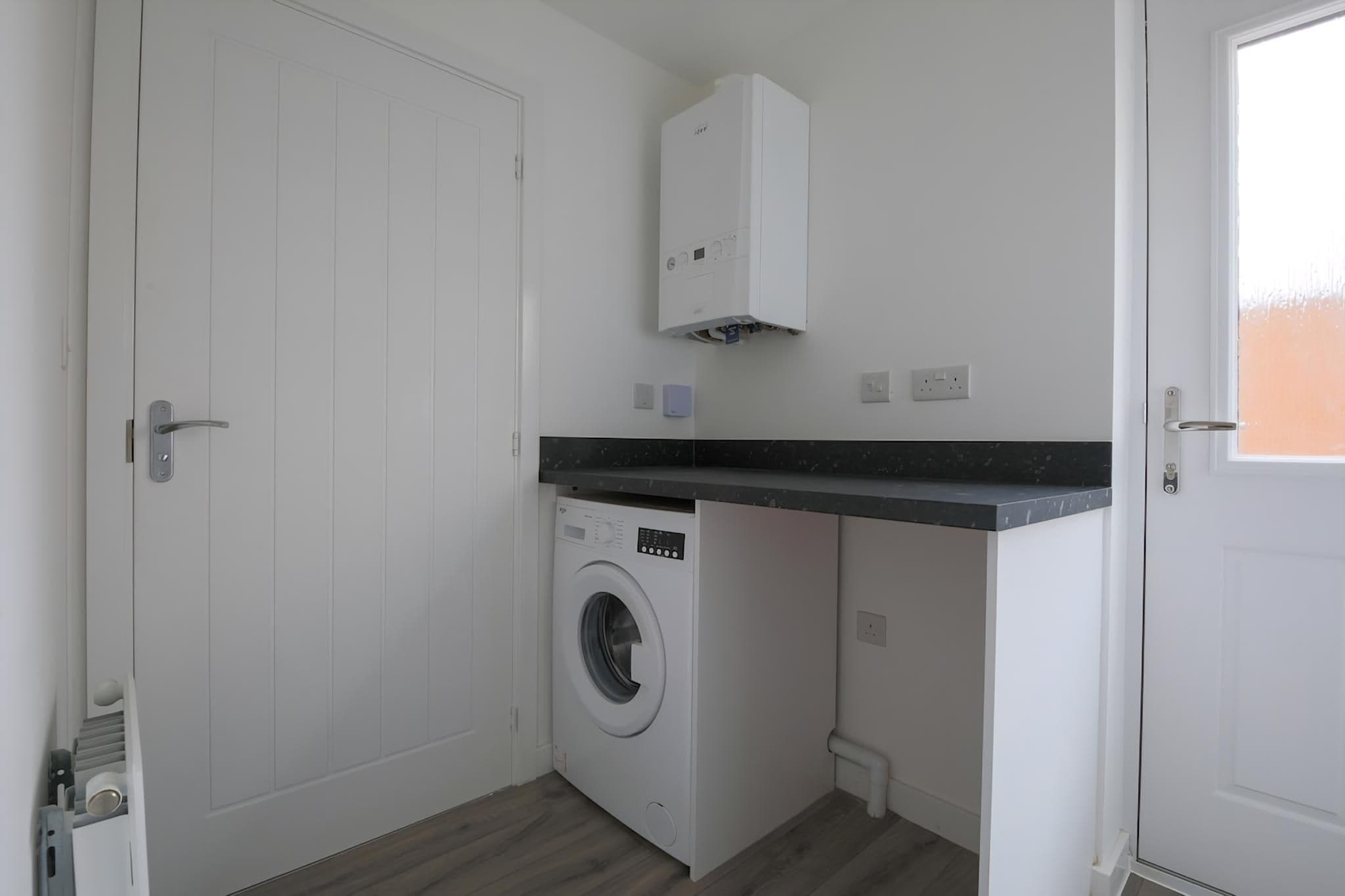 A compact laundry room with a washing machine, a small cabinet, and a door.
