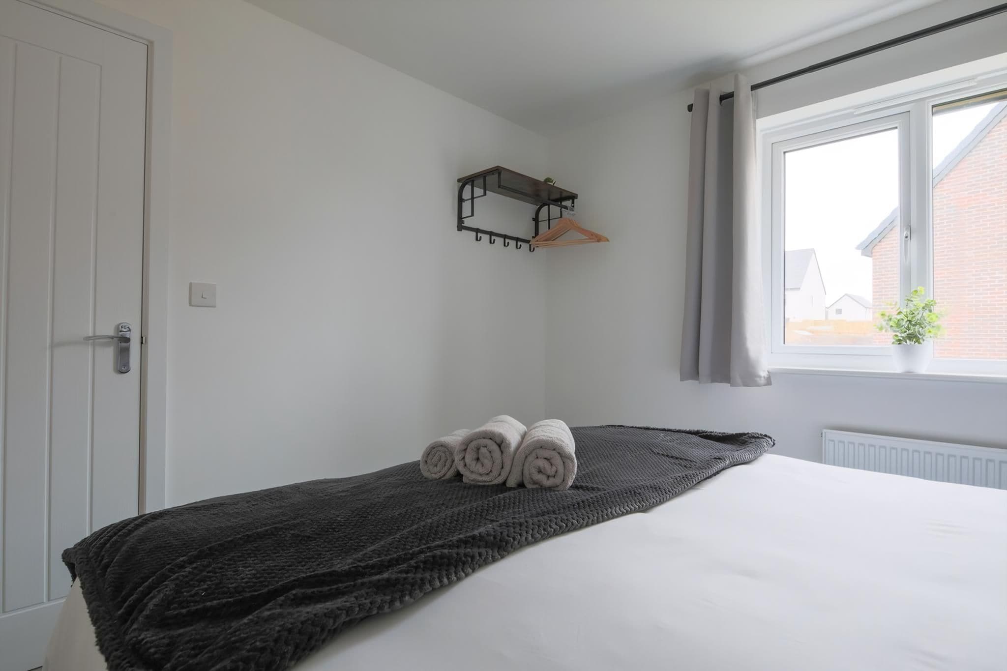 A bedroom with a bed, a dark blanket, a towel, a hanging rack, and a window with a view.