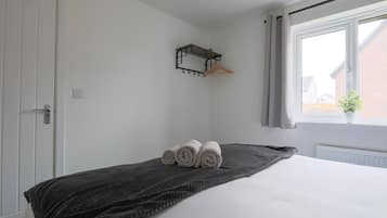 Un dormitorio con una cama, una manta oscura, una toalla, un perchero y una ventana con vistas.