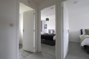Un dormitorio con una cama, una mesita de noche, una lámpara y una puerta que da a otra habitación.