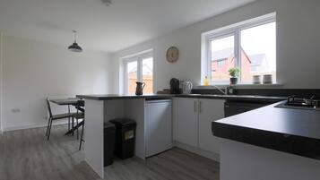 A modern kitchen with white cabinets, a black countertop, a dining area with a chair, and a window with a view of buildings.