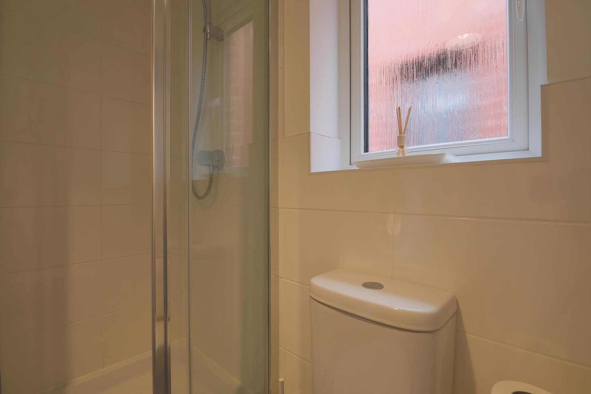A bathroom with a glass shower enclosure, a toilet, and a window with a view of the outside.
