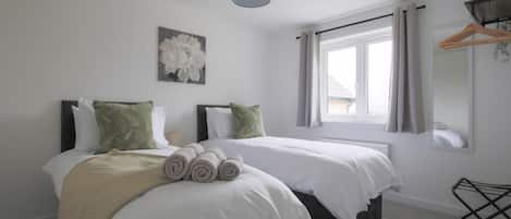 Habitación de hotel con dos camas, una lámpara colgante, una ventana con cortinas, un espejo adosado a la pared y un tendedero.