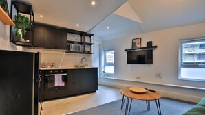 A modern kitchen with a black refrigerator, built-in oven, and microwave. There is a small dining table with a wooden top and metal legs. - Modern 1-bed Flat Near Cardiff City Centre (Cardiff)