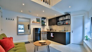 A modern living room with a green sofa, a round coffee table, and a kitchen area with dark cabinetry and a built-in oven. - Modern 1-bed Flat Near Cardiff City Centre (Cardiff)