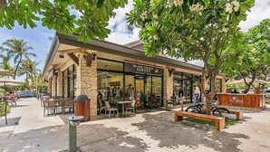 A coffee shop with outdoor seating, stone facade, and palm trees.