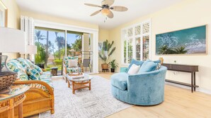 A spacious living room with a large window, a ceiling fan, and a view of palm trees.