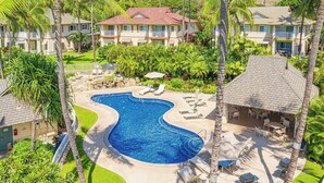 A resort with a large swimming pool, lounge chairs, and palm trees.