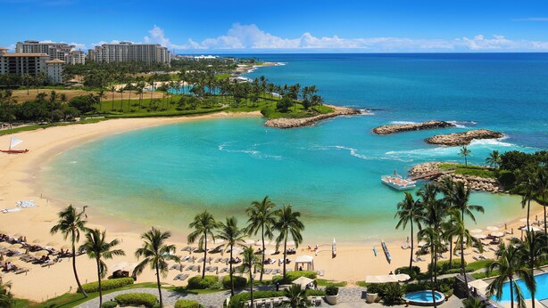 A resort with a beach, clear turquoise waters, and palm trees.